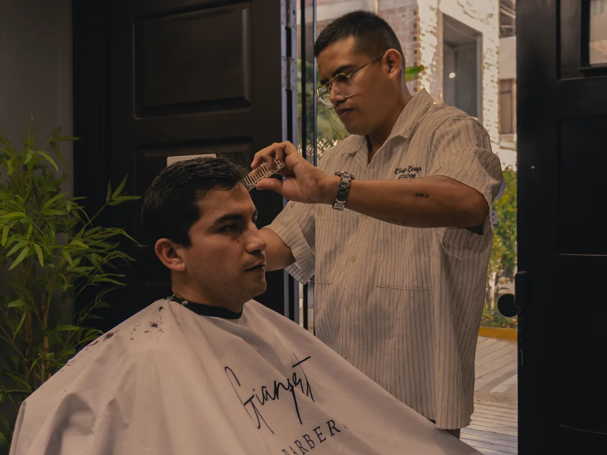 Gianpiert peinando y cortando el cabello de un cliente en la barbería